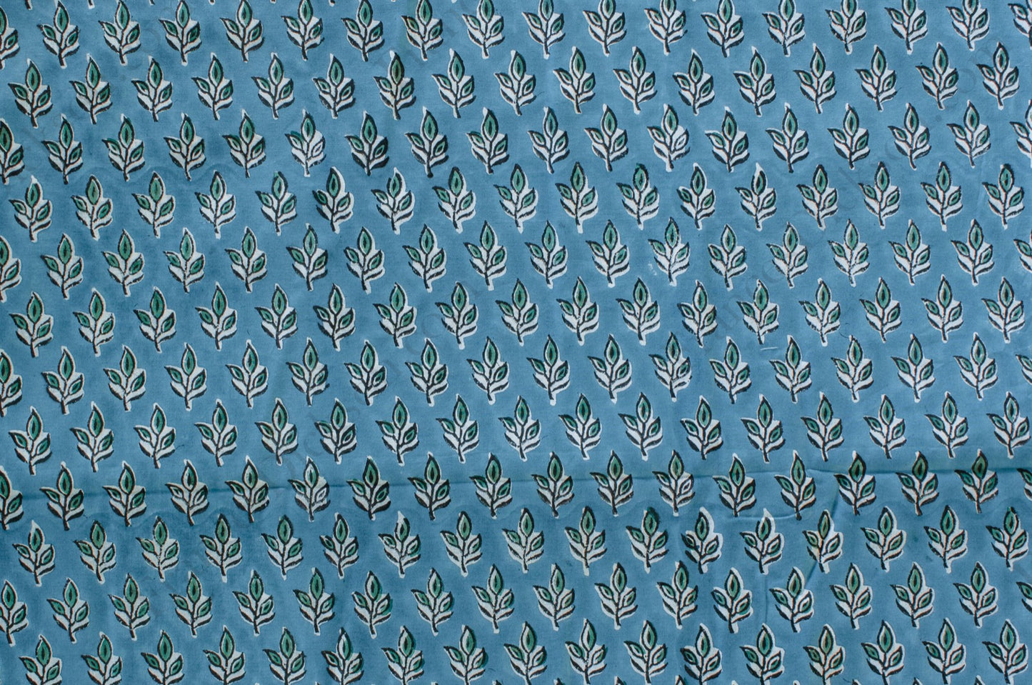 Blue cotton fabric with green floral block print and white accents, handmade in Jaipur, India using traditional artisan techniques.