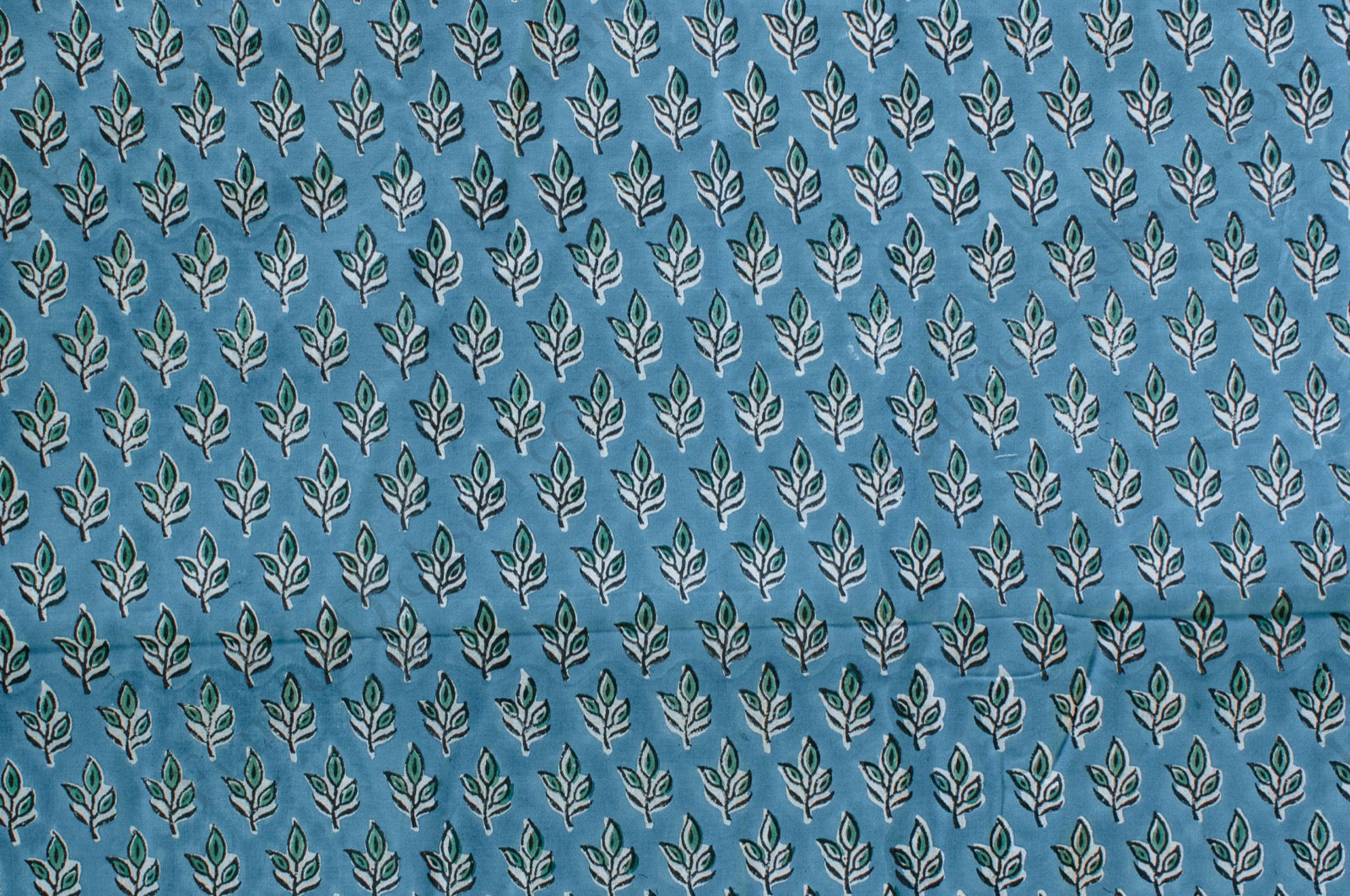Blue cotton fabric with green floral block print and white accents, handmade in Jaipur, India using traditional artisan techniques.