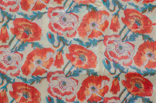 White cotton fabric hand block printed with orange, red, and blue floral motifs, handcrafted by artisans in Jaipur, India.