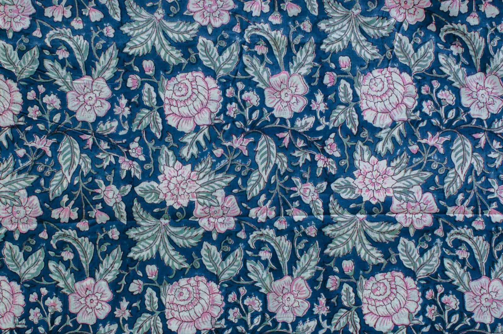 Blue cotton fabric with hand block printed pink blossoms and green leaves, crafted by artisans in Jaipur, India using traditional methods.