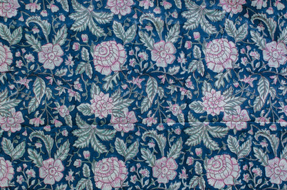 Blue cotton fabric with hand block printed pink blossoms and green leaves, crafted by artisans in Jaipur, India using traditional methods.