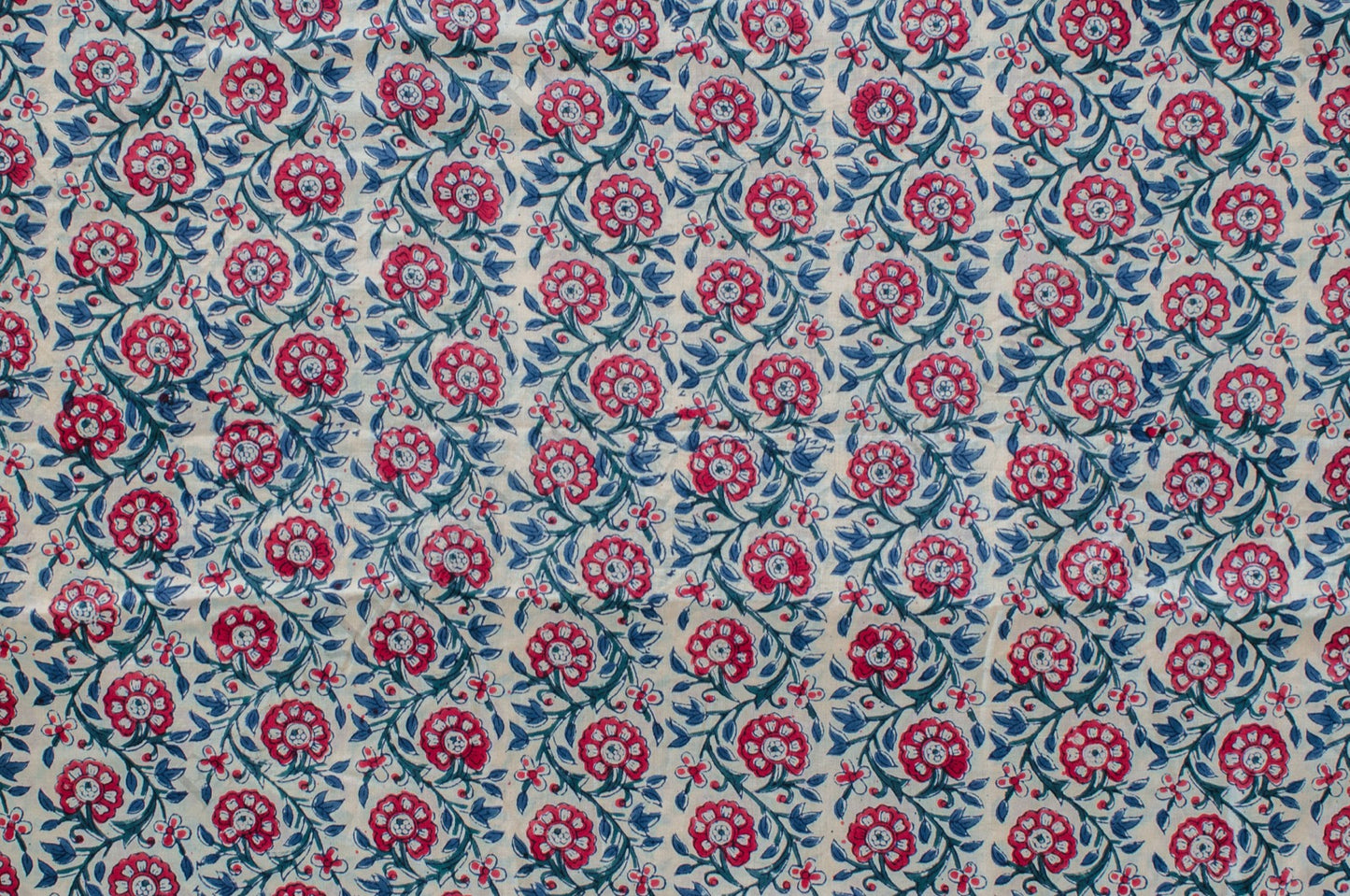 Hand block printed cotton fabric featuring a red, blue, and green floral motif on white, made by artisans in Jaipur, India.