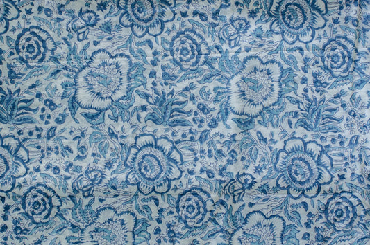 White cotton fabric with soft blue hand block printed floral motifs, handcrafted by artisans in Jaipur, India using traditional methods.