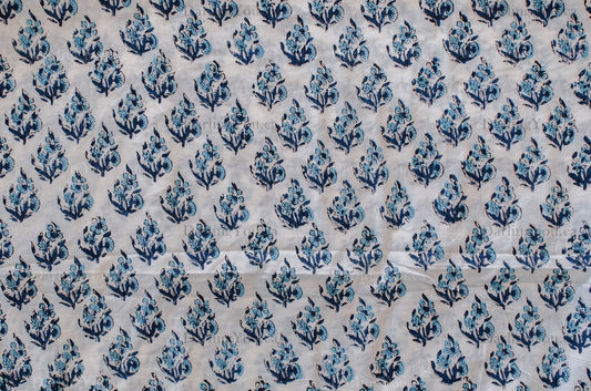 White cotton fabric featuring blue hand block printed floral design, traditionally crafted by artisans in Jaipur, India.