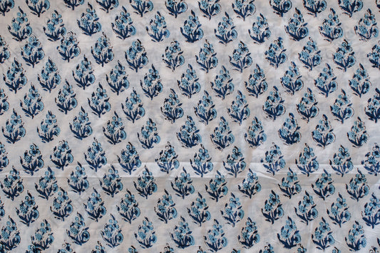 White cotton fabric featuring blue hand block printed floral design, traditionally crafted by artisans in Jaipur, India.