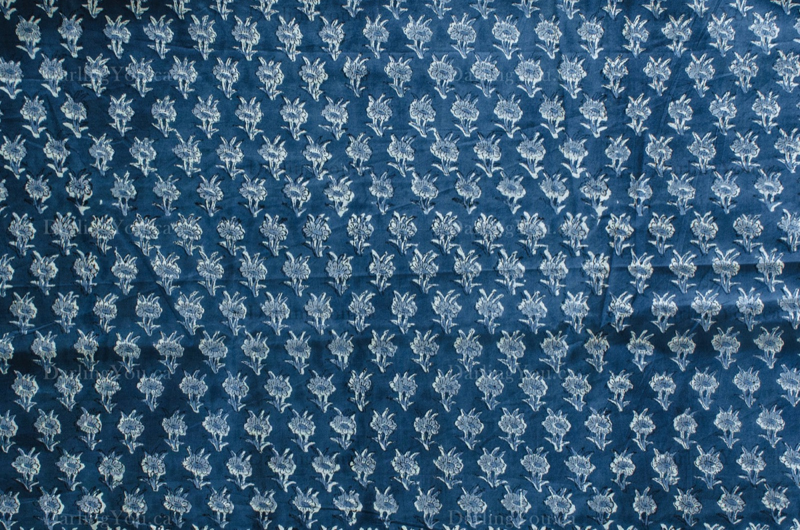Close-up of hand block-printed cotton voile fabric with repeating white floral motifs on a deep blue background, made in Jaipur, India.