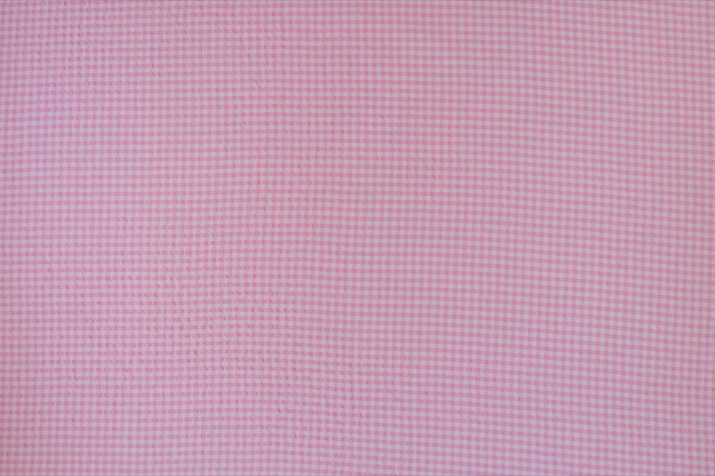 Organic yarn-dyed cotton seersucker fabric featuring candy pink micro gingham check with lightweight puckered texture.