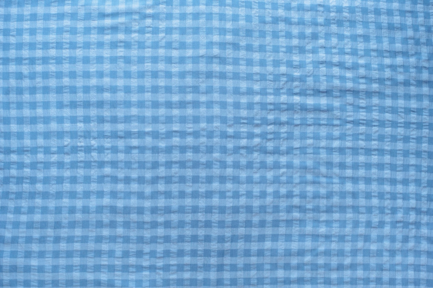 Dark and light blue gingham organic cotton fabric with seersucker texture, folded to show puckered weave and pattern.