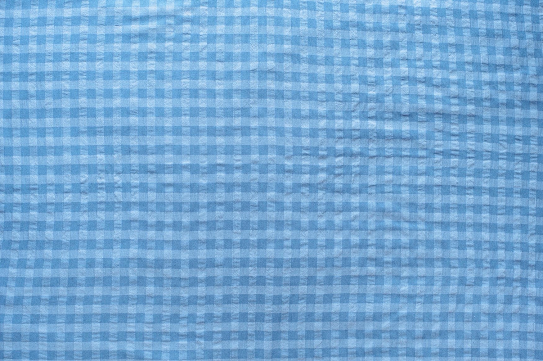 Dark and light blue gingham organic cotton fabric with seersucker texture, folded to show puckered weave and pattern.