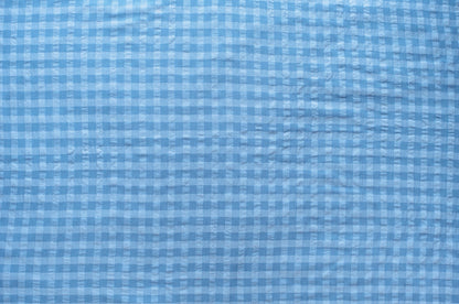 Dark and light blue gingham organic cotton fabric with seersucker texture, folded to show puckered weave and pattern.