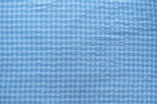 Dark and light blue gingham organic cotton fabric with seersucker texture, folded to show puckered weave and pattern.