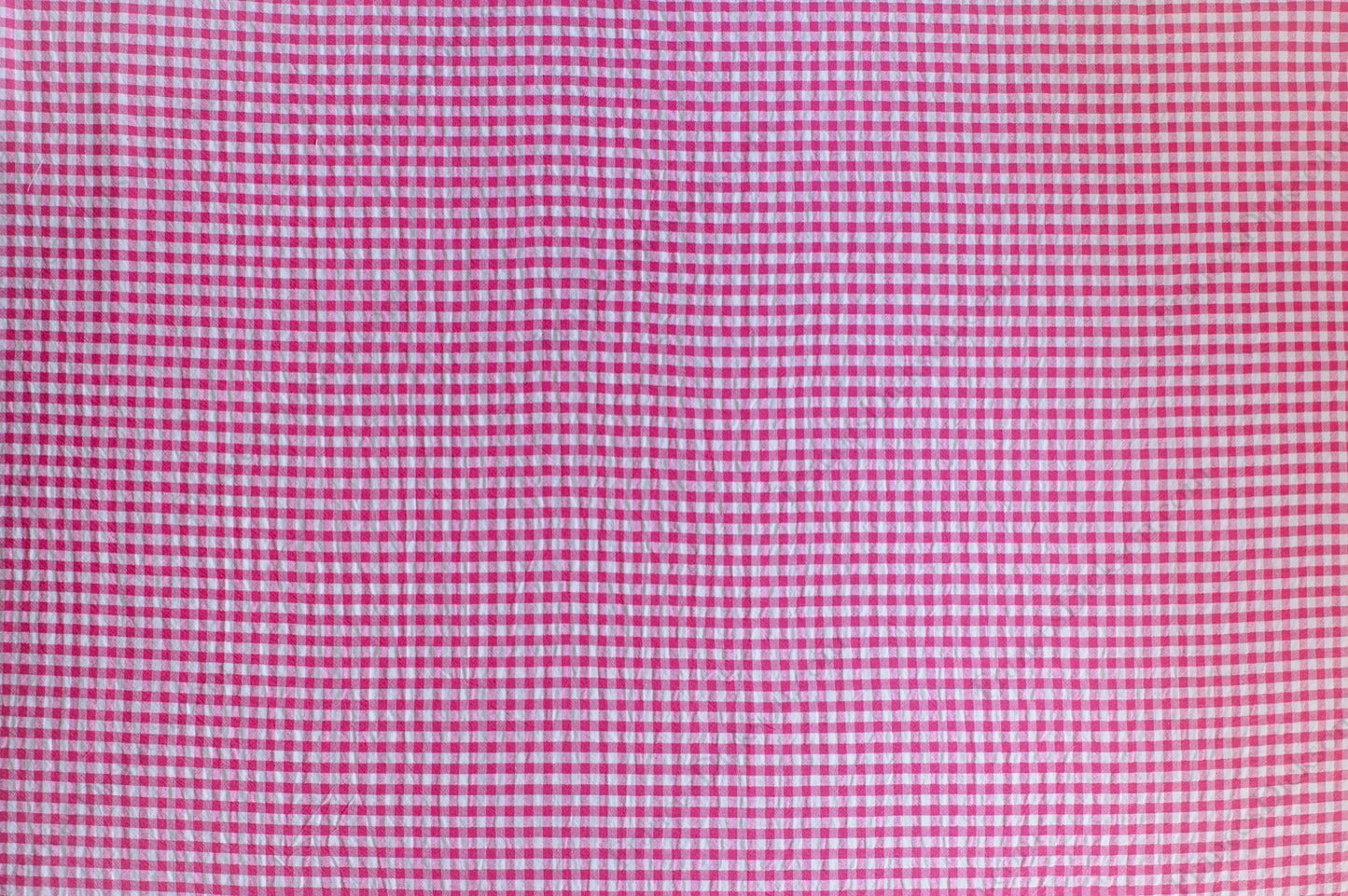 Fuchsia and pink gingham organic cotton fabric with seersucker texture, folded to show puckered weave and pattern.