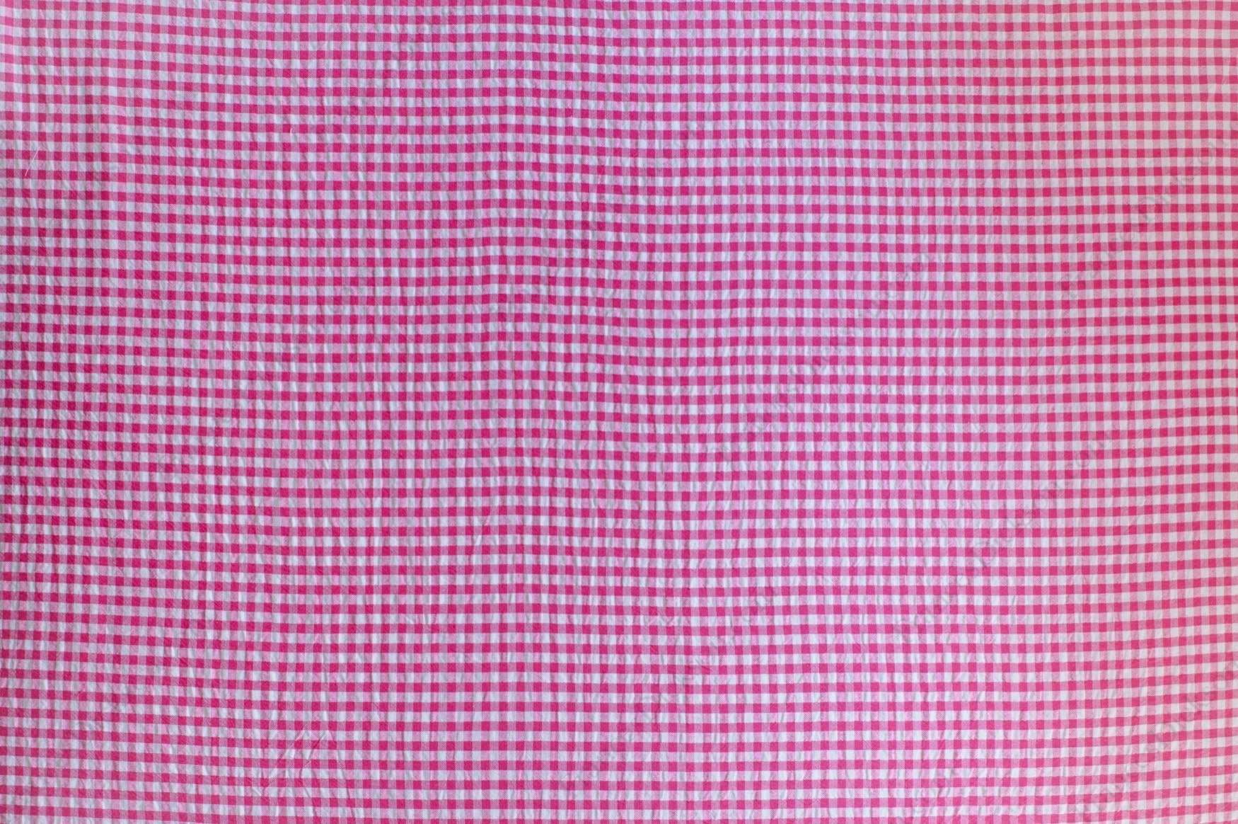 Fuchsia and pink gingham organic cotton fabric with seersucker texture, folded to show puckered weave and pattern.