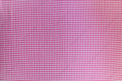 Fuchsia and pink gingham organic cotton fabric with seersucker texture, folded to show puckered weave and pattern.