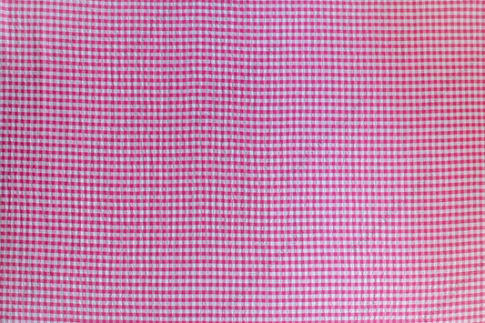 Fuchsia and pink gingham organic cotton fabric with seersucker texture, folded to show puckered weave and pattern.