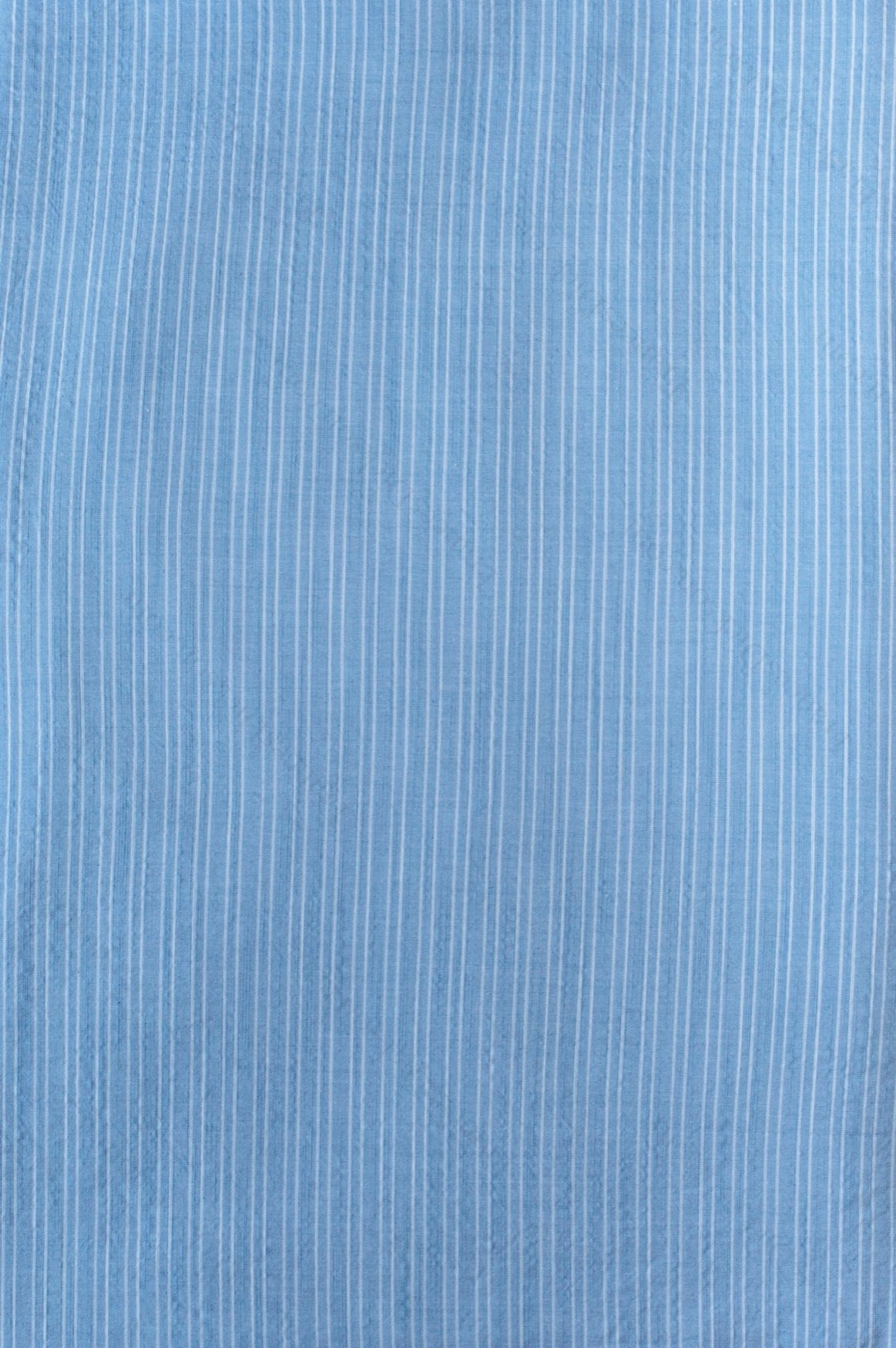 Light blue organic cotton shirting fabric with subtle two-tone blue yarn-dyed stripe pattern, folded to show texture and weave.