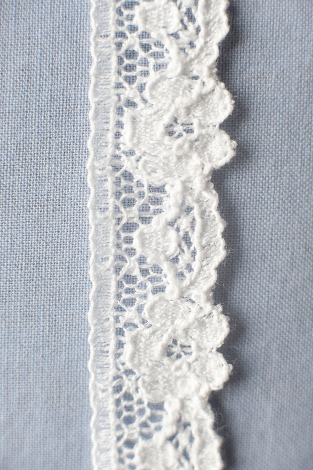 Off-white cotton lace trim with raised floral motifs and scalloped edge, featuring delicate openwork detail.