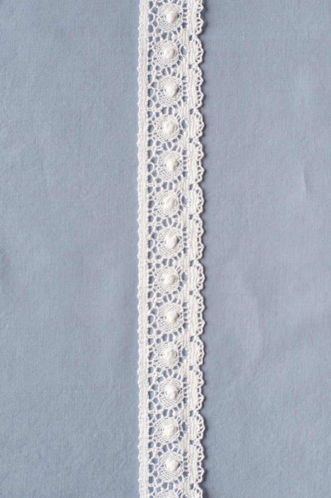 Off-white cotton lace with repeating circular medallion motifs and scalloped edges, showing intricate openwork pattern.