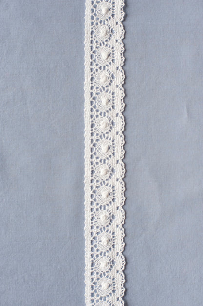 Off-white cotton lace with repeating circular medallion motifs and scalloped edges, showing intricate openwork pattern.