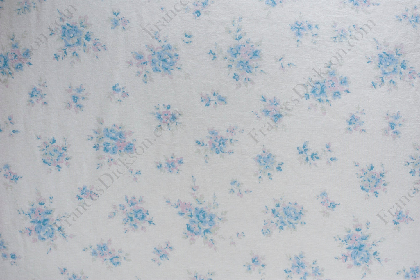 Organic cotton cambric fabric with scattered powder blue and blush pink floral bouquets on an ivory background, shown flat and draped on a dress form.