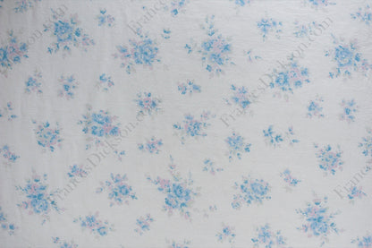 Organic cotton cambric fabric with scattered powder blue and blush pink floral bouquets on an ivory background, shown flat and draped on a dress form.