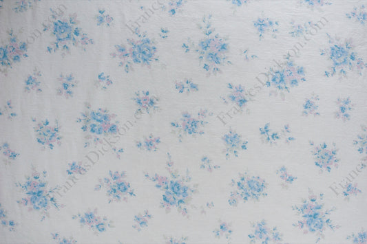 Organic cotton cambric fabric with scattered powder blue and blush pink floral bouquets on an ivory background, shown flat and draped on a dress form.