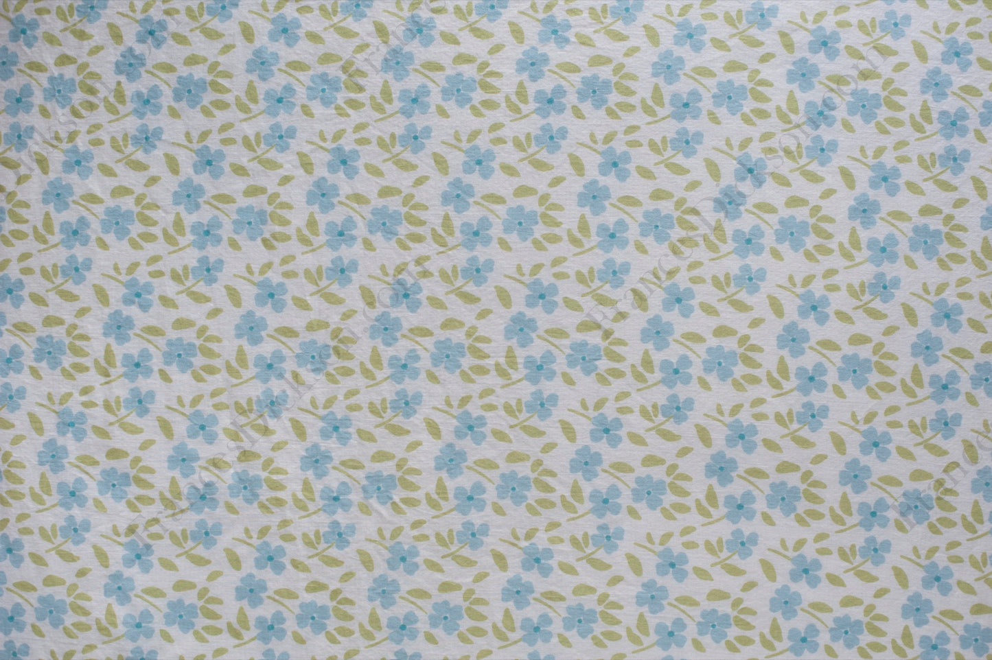 Organic cotton voile fabric with small blue flowers and green leaves scattered across a white background in a ditsy floral print.